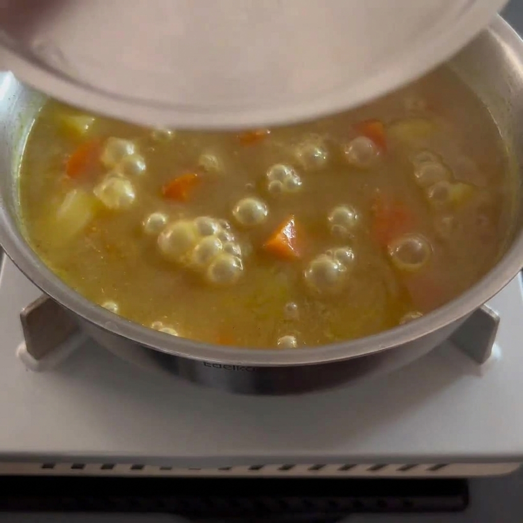 부드러운 감자와 당근 조각이 보이는 진한 황금빛 갈색 카레 소스를 젓는 모습.