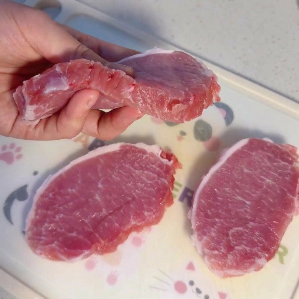 도마 위에 놓인 두툼하게 썬 생 돼지고기 등심 조각.