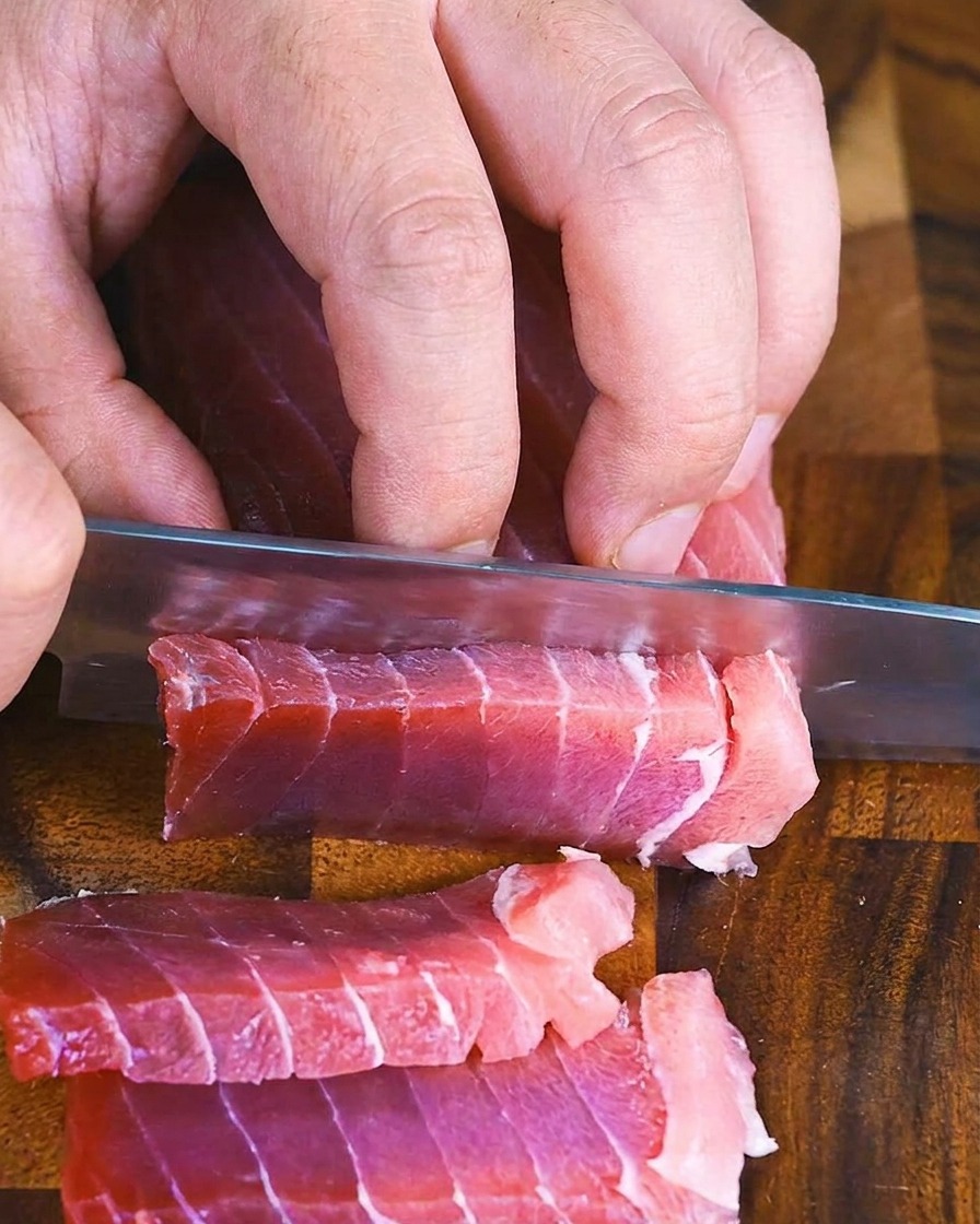 도마 위에서 날카로운 칼로 참치 블록을 두툼하고 고르게 써는 모습.