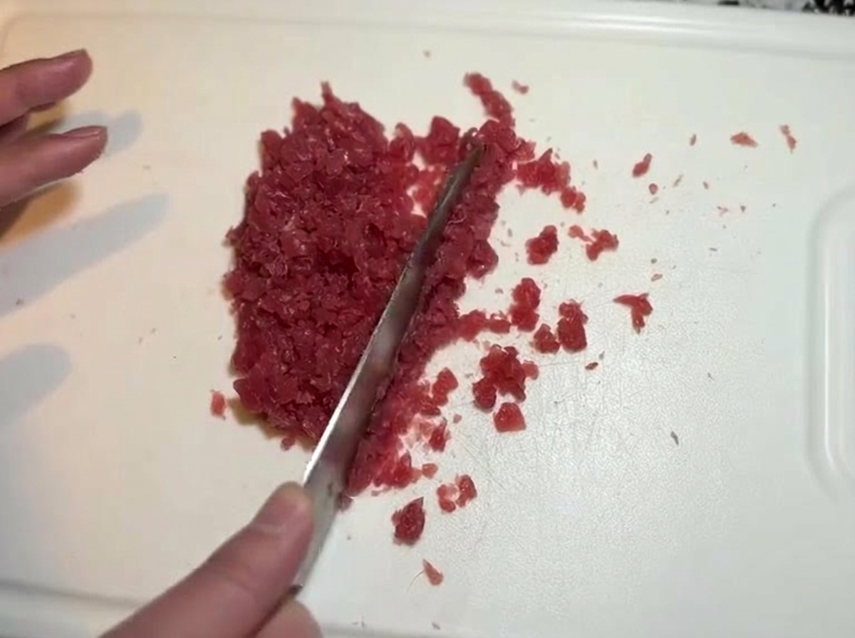 도마 위에서 칼로 붉은 생참치 조각들을 잘게 써는 모습.