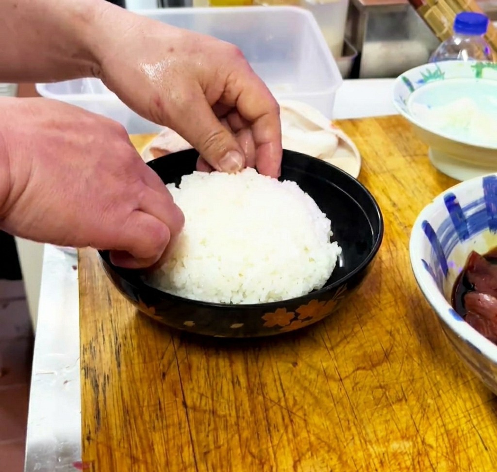 검은색 그릇에 갓 지은 흰쌀밥을 평평하게 담는 모습.