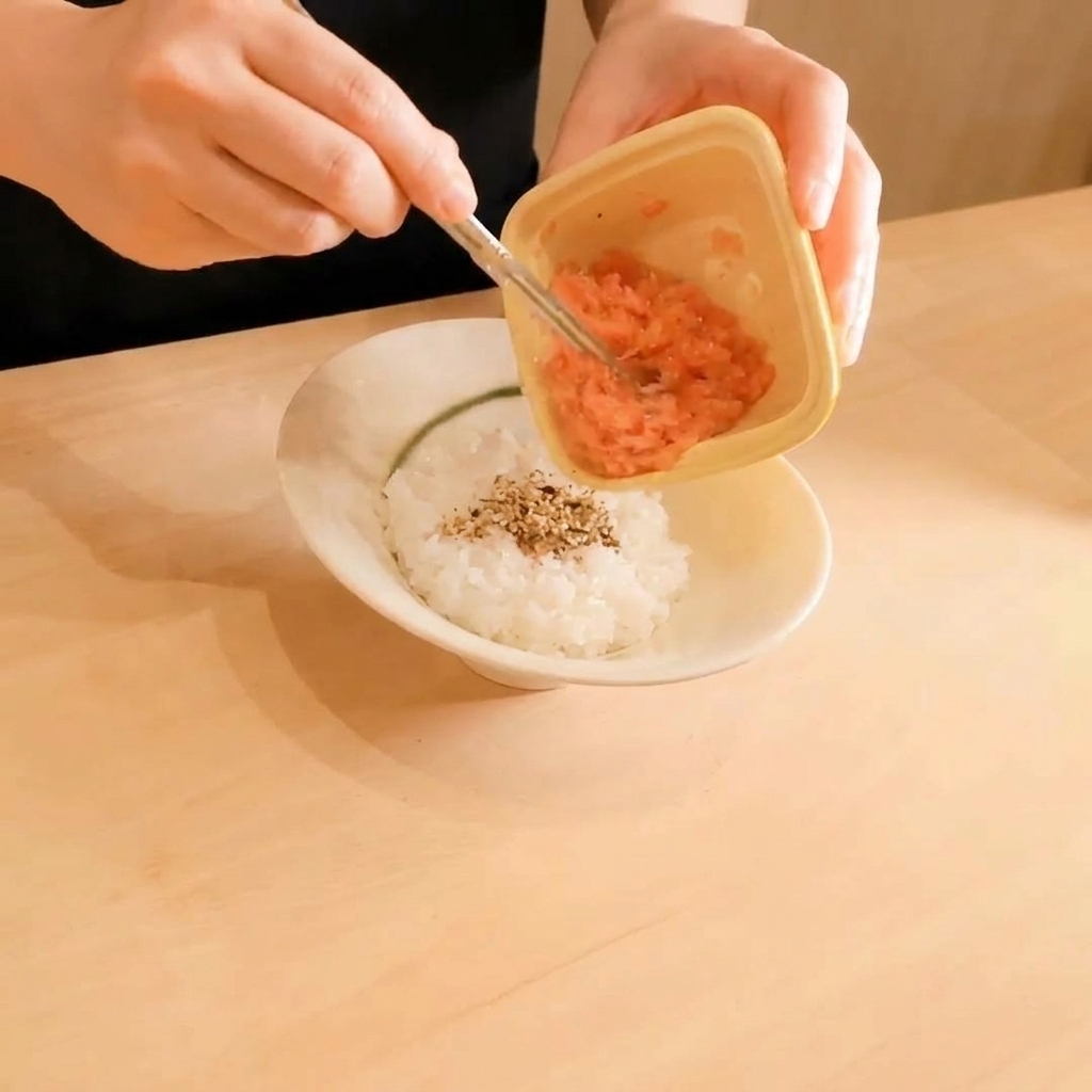 참깨가 뿌려진 흰 밥 위에 작은 플라스틱 용기에 담긴 다진 생참치를 덜어내는 모습.