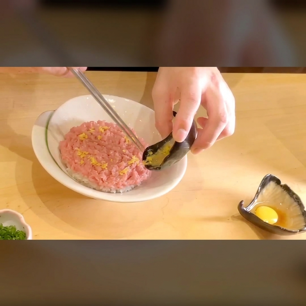 밥 위의 다진 참치 옆에 선명한 노란색 단무지를 올리는 클로즈업 장면.