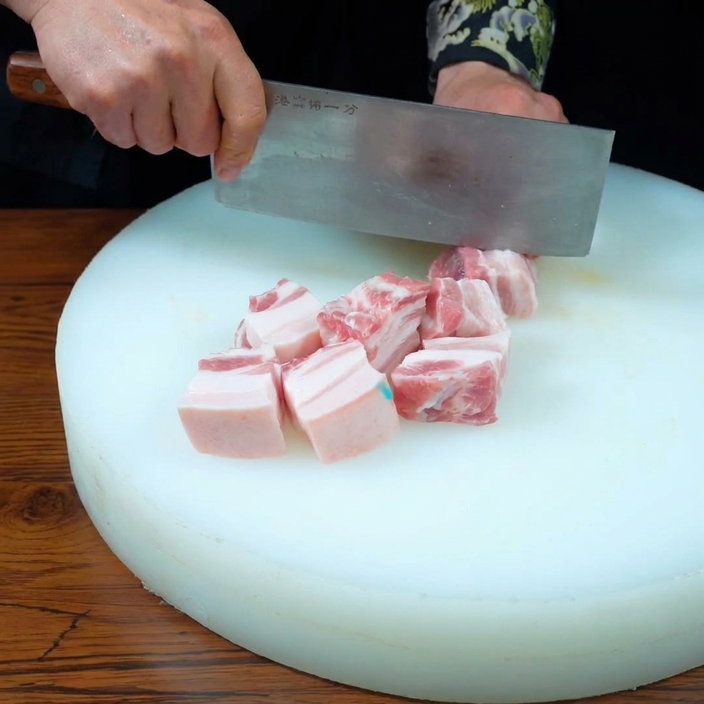 흰색 도마 위에서 식칼을 사용해 세 겹의 삼겹살을 일정한 크기로 써는 모습.