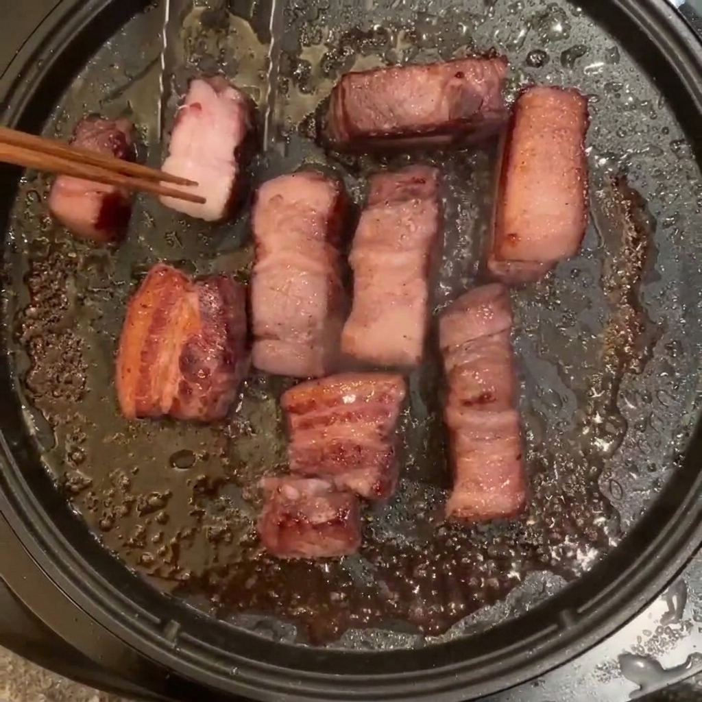 팬에서 구워지고 있는 여러 조각의 삼겹살을 나무젓가락으로 뒤집는 모습.