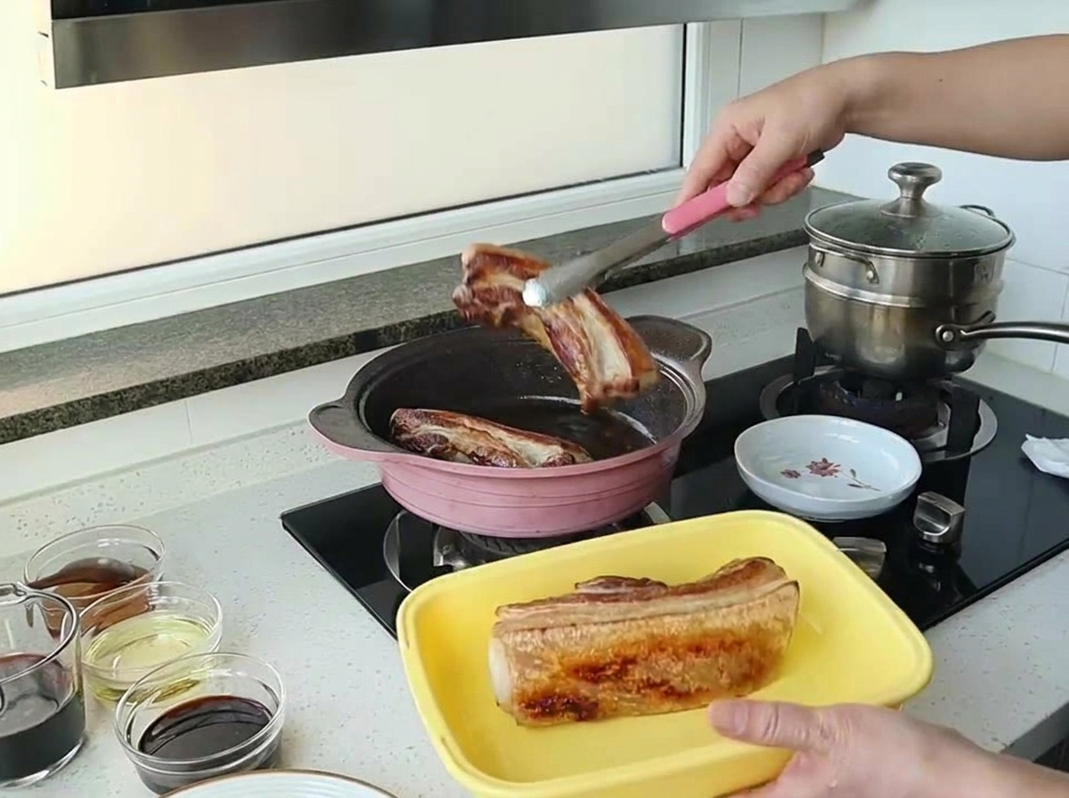 분홍색 팬에서 잘 구워진 삼겹살을 집게로 들어 올리는 모습.