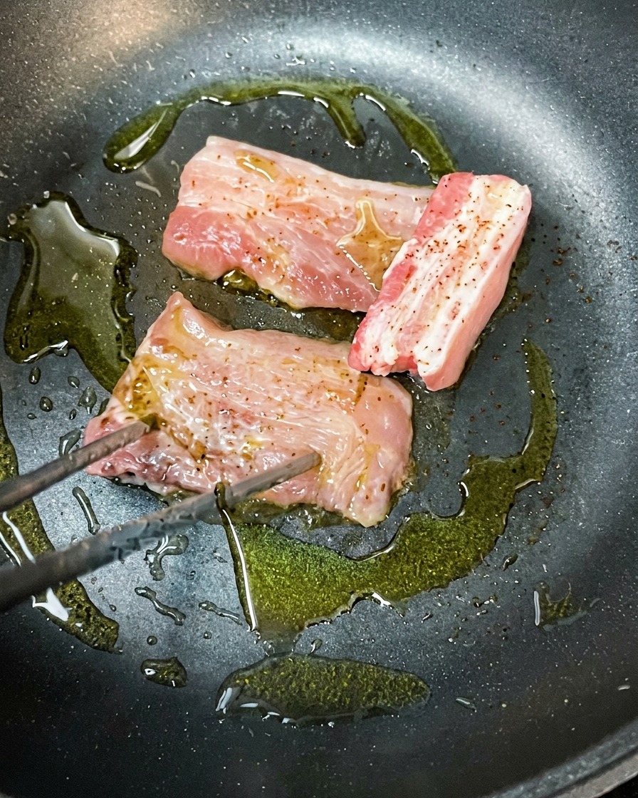 달궈진 팬에서 올리브 오일과 함께 삼겹살이 노릇하게 구워지는 모습.
