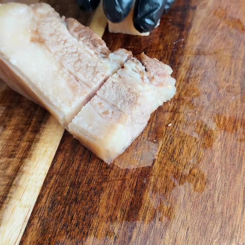 도마 위에서 식힌 통삼겹살을 일정한 사각형 모양으로 써는 모습.