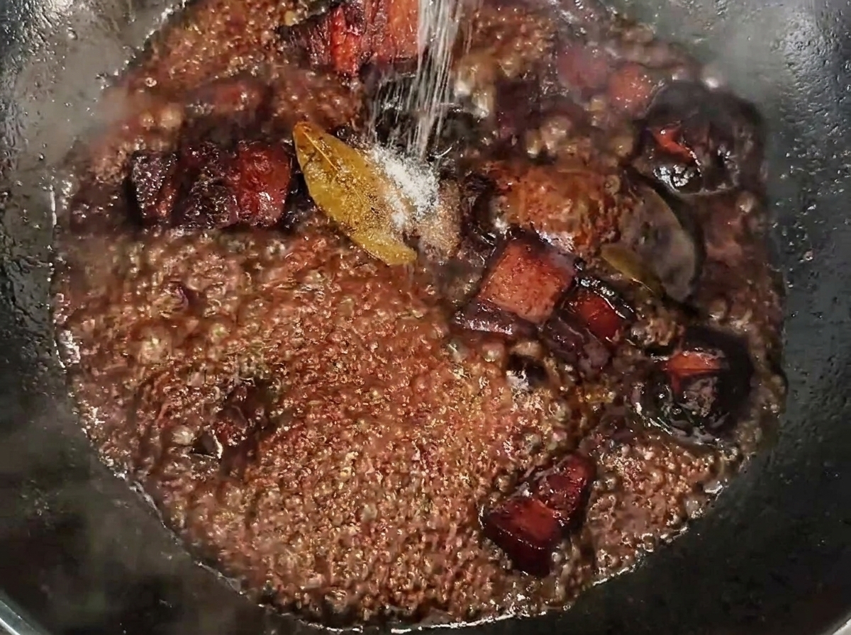 진한 소스에 졸여지는 통삼겹살 위로 소금을 뿌리는 모습.