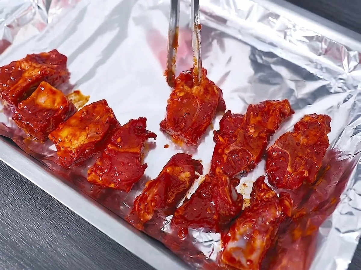 알루미늄 호일을 깐 오븐 트레이에 집게로 marinated 돼지갈비를 일렬로 놓는 모습.