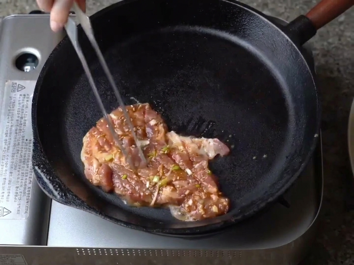 뜨겁게 달군 무쇠 팬에 양념된 돼지고기 한 점을 올리는 모습.