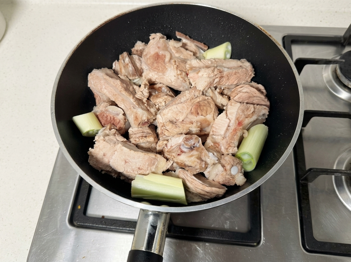 검은 팬에 담긴 생 돼지갈비와 대파 조각들.
