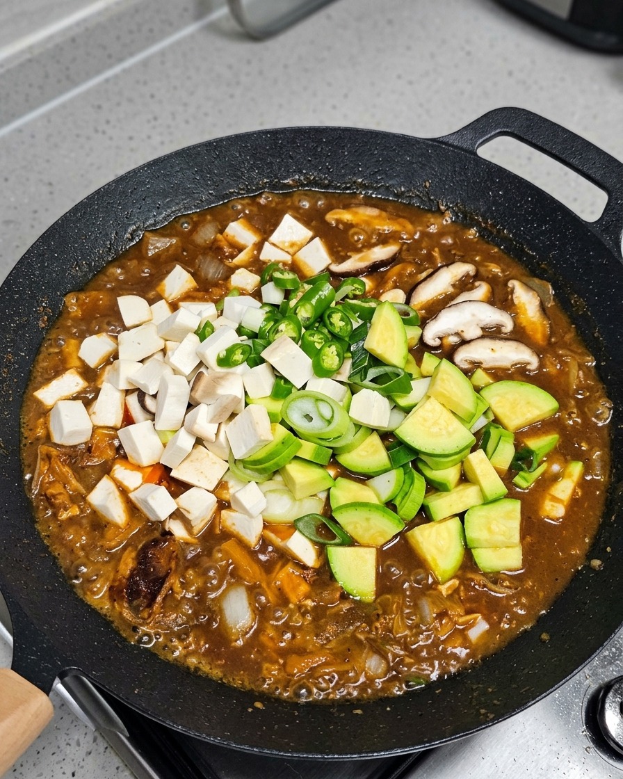 끓는 찌개에 애호박, 두부, 버섯, 고추를 넣는 모습.