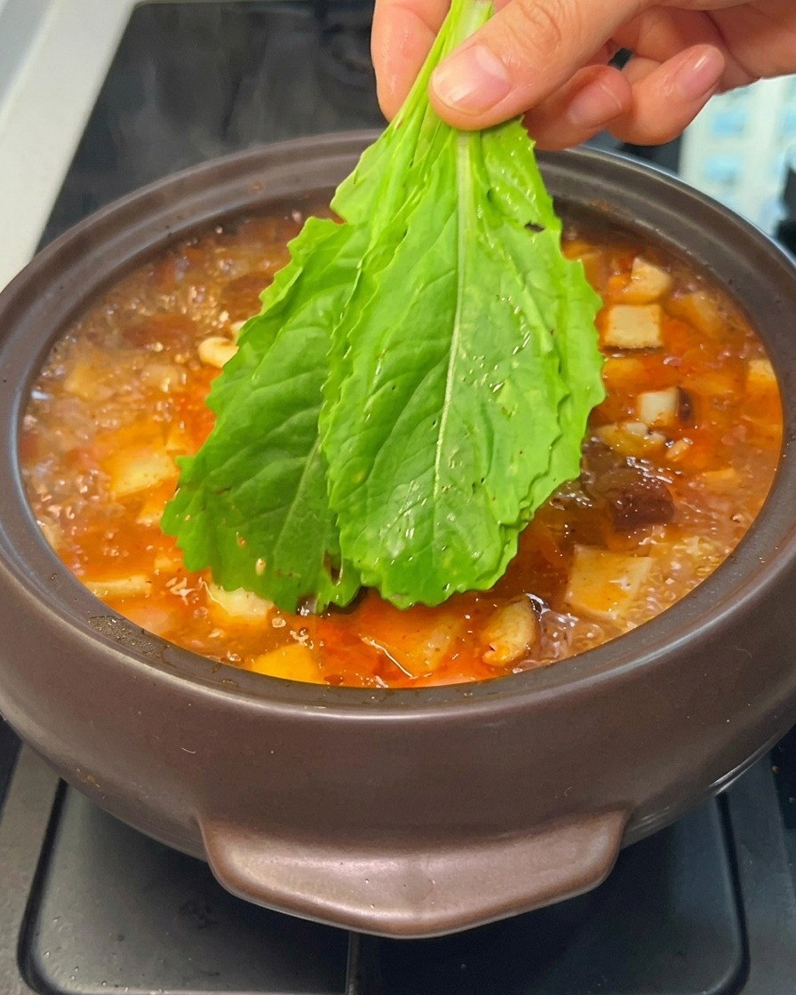 찌개 위에 시금치 등의 잎채소를 올리는 모습.