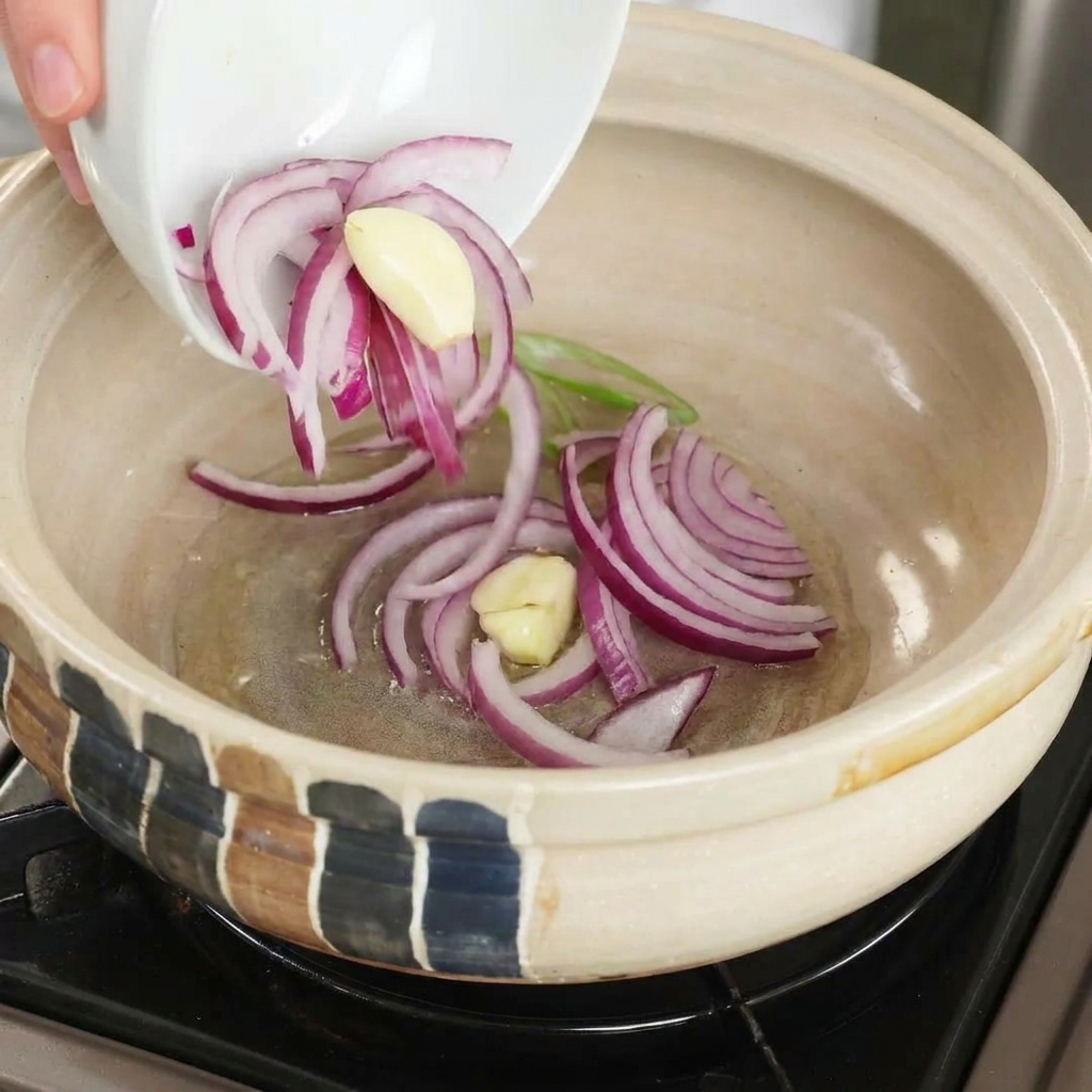 달궈진 뚝배기에 슬라이스한 적양파와 마늘을 넣고 볶는 모습.