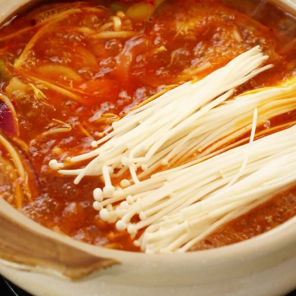 팔팔 끓는 붉은 국물에 팽이버섯과 두부를 넣는 모습.