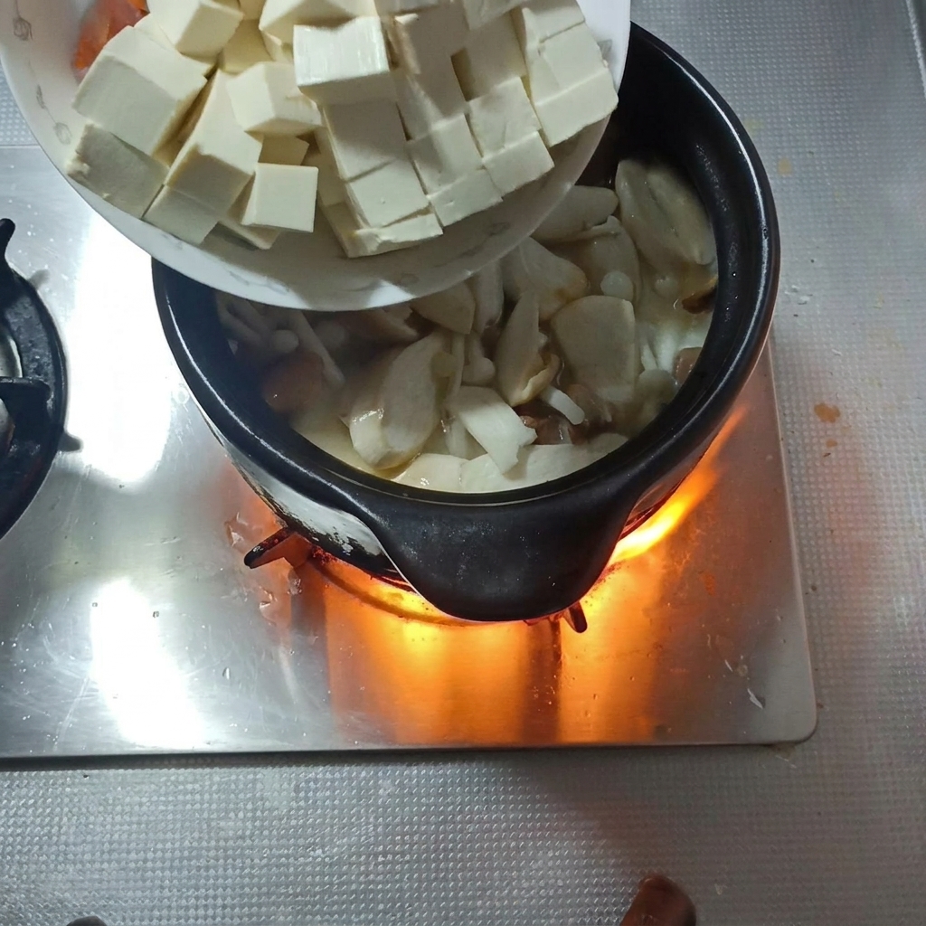 깍둑썰기한 연두부와 당근채를 버섯 국물에 넣는 모습.