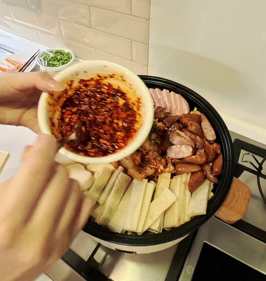 재료가 담긴 부대찌개 냄비 한가운데에 붉은 양념장을 얹는 모습