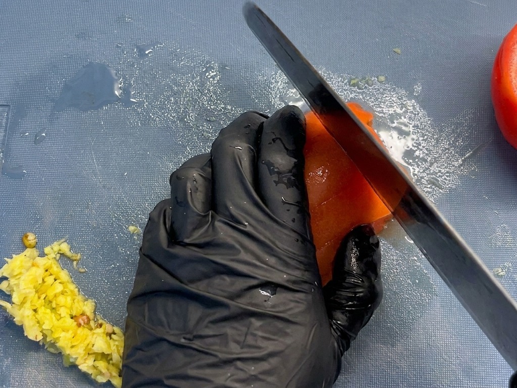 파란색 도마 위에서 껍질을 벗긴 토마토를 일정한 크기로 써는 모습.