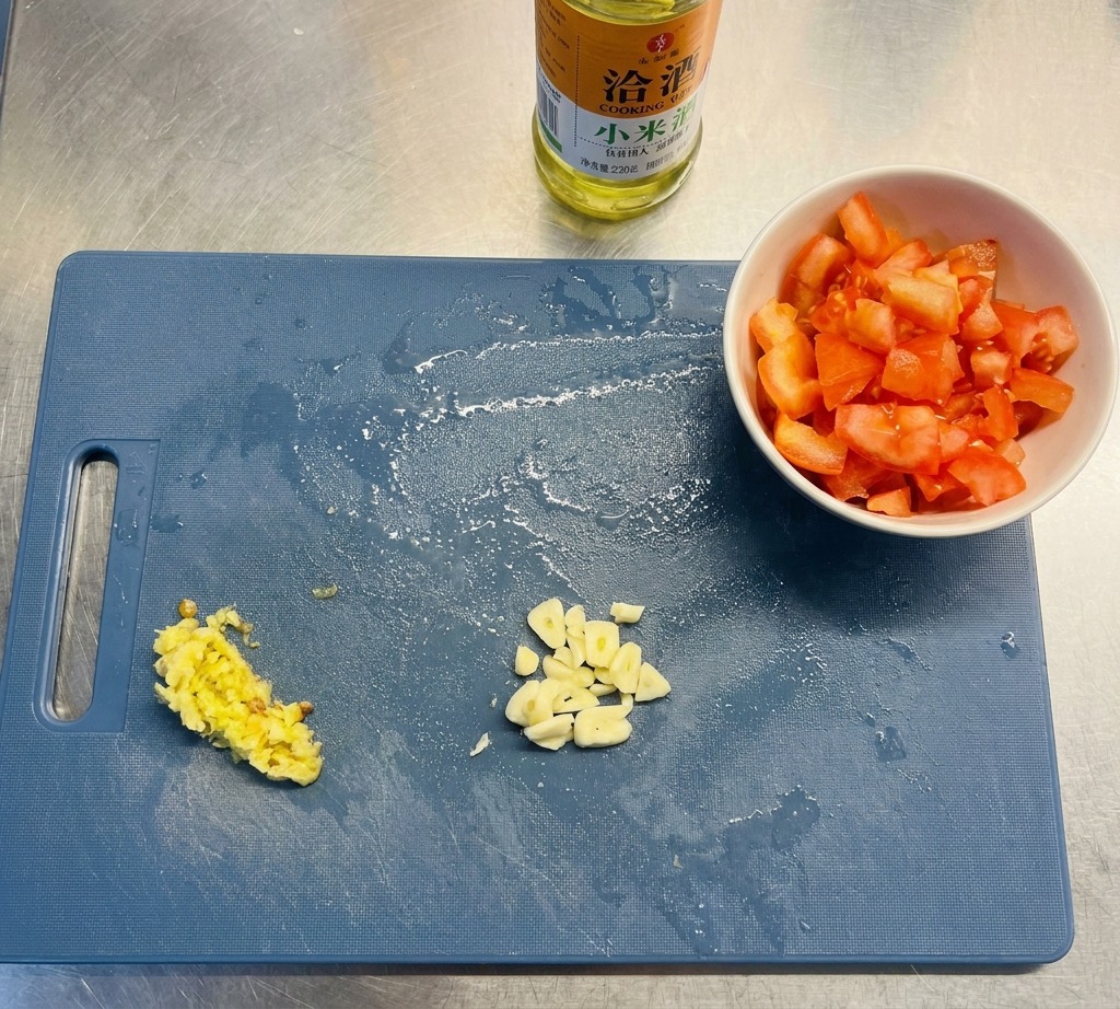 파란색 도마 위에 마늘 슬라이스, 다진 고추, 다진 토마토가 나란히 놓여 있는 모습.
