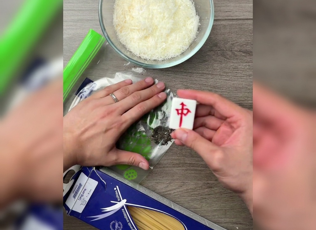 주방 조리대 위 비닐봉지에 담긴 통후추를 마작 패처럼 평평한 도구로 으깨는 모습.