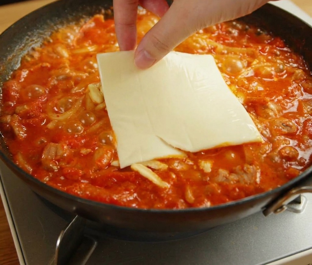 녹고 있는 모짜렐라와 우동 위에 노란 체다 슬라이스 치즈 한 장을 올리는 모습.