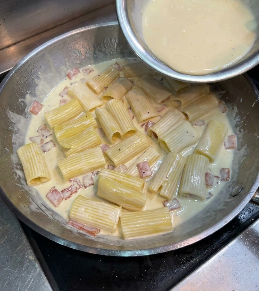 팬 안의 리가토니 위로 연노란색 달걀 치즈 혼합물을 붓고 있는 모습.