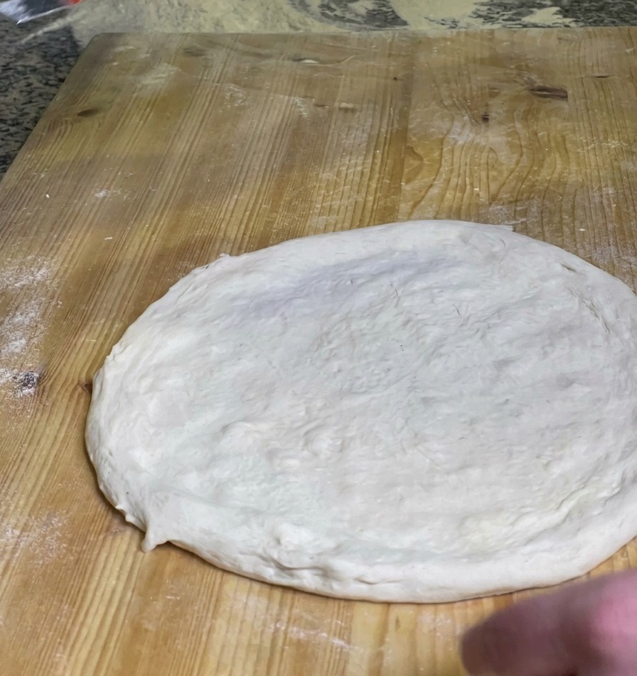 나무 도마 위에서 둥글게 편 피자 도우 중앙에 선명한 붉은 토마토 소스를 펴 바르는 셰프의 모습