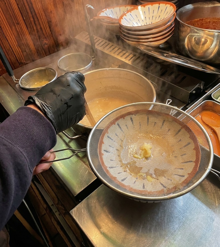 김이 모락모락 나는 뽀얀 사골 육수가 거름망을 거쳐 화려한 라멘 그릇에 담기는 모습.