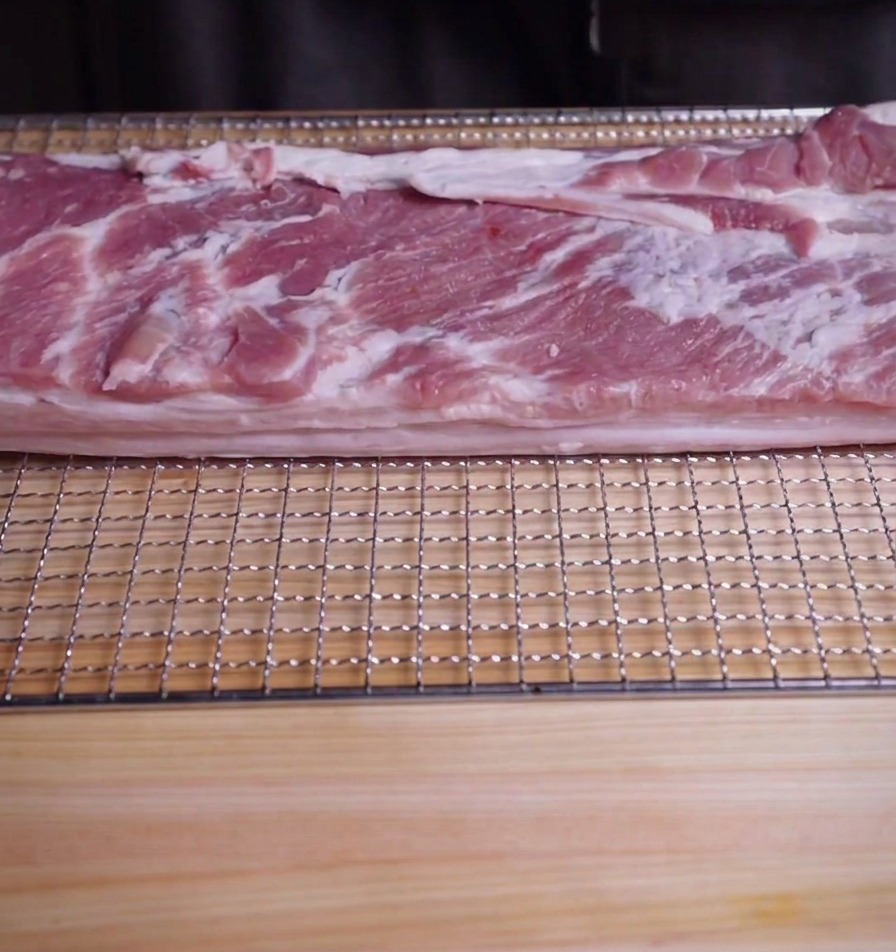 도마 위 석쇠에 놓인 신선한 통삼겹살 덩어리.