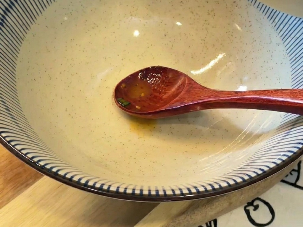 작은 그릇에 담긴 뽀얀 주황색 국물을 파란색 줄무늬가 있는 큰 라면 그릇에 붓는 모습.