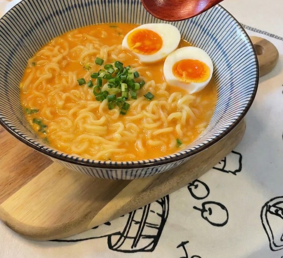 계란과 파가 올려진 라면 그릇 위에 나무 숟가락을 들고 있는 모습.