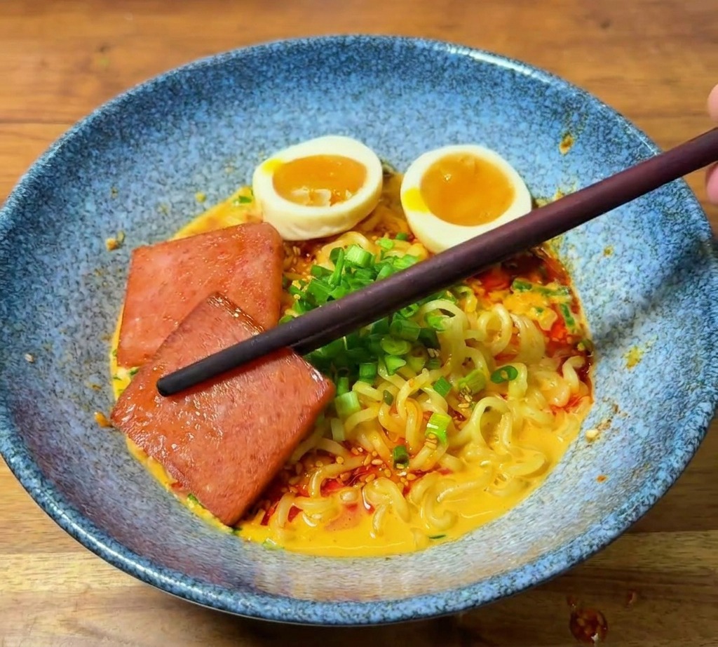 젓가락으로 노릇하게 구운 런천미트 한 조각을 그릇 가장자리에 배치하는 모습.