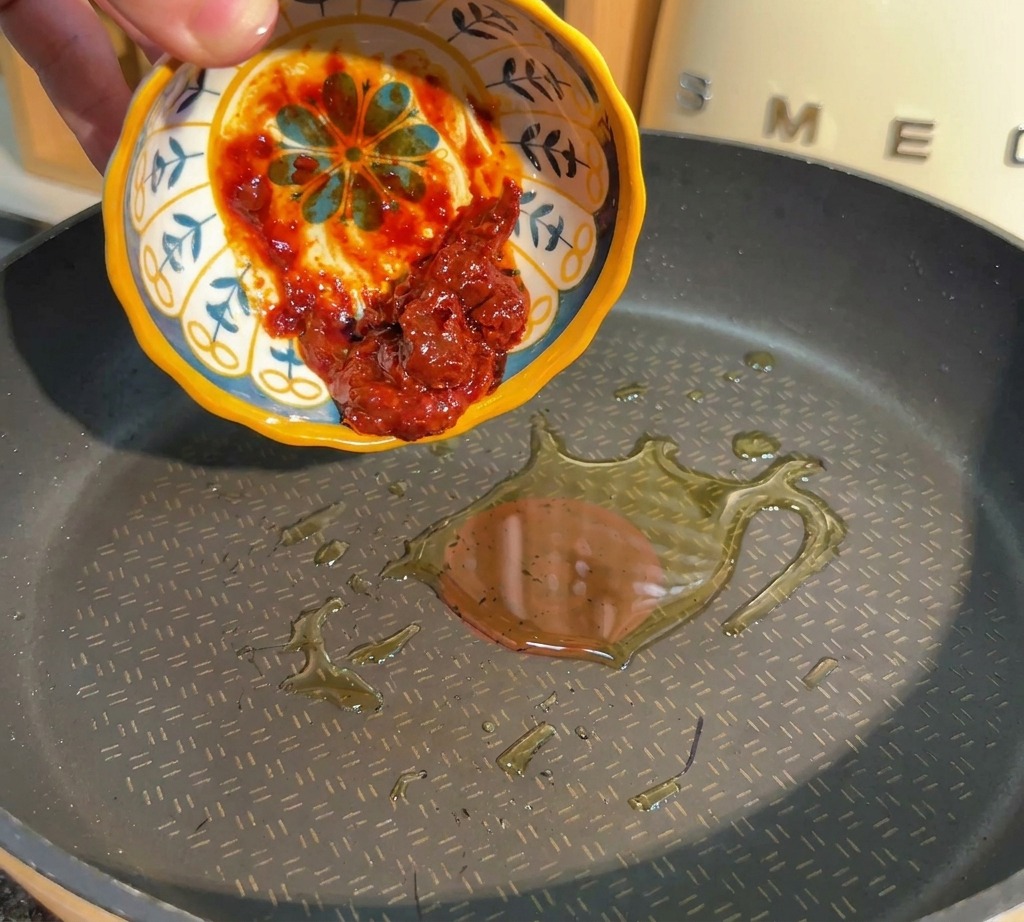 손으로 패턴 무늬 그릇에 담긴 붉은 두반장을 달궈진 기름에 넣는 모습