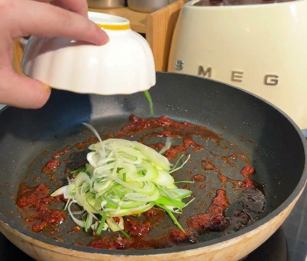 붉은 소스 베이스가 담긴 팬에 채 썬 대파를 추가하는 모습