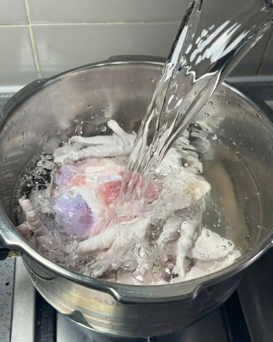 사골 뼈와 닭발이 담긴 냄비에 깨끗한 물을 붓는 모습.