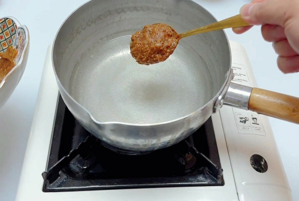 냄비에 담긴 맑은 물 위로 숟가락에 가득 담긴 미소 양념장을 넣으려는 모습.