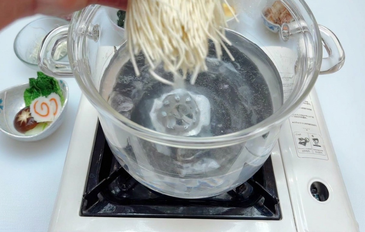 끓는 물이 담긴 냄비에 하얀 라멘 면 한 뭉치를 조심스럽게 넣는 모습.