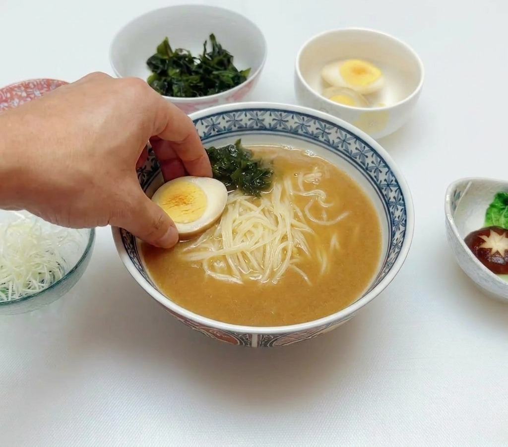 면과 미역이 담긴 라멘 그릇 위에 반으로 자른 반숙 달걀을 조심스럽게 놓는 모습.