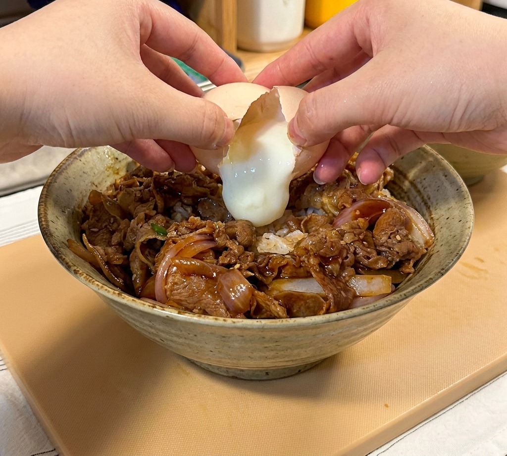 소고기 덮밥 중앙에 조심스럽게 온센타마고를 깨서 올리는 모습