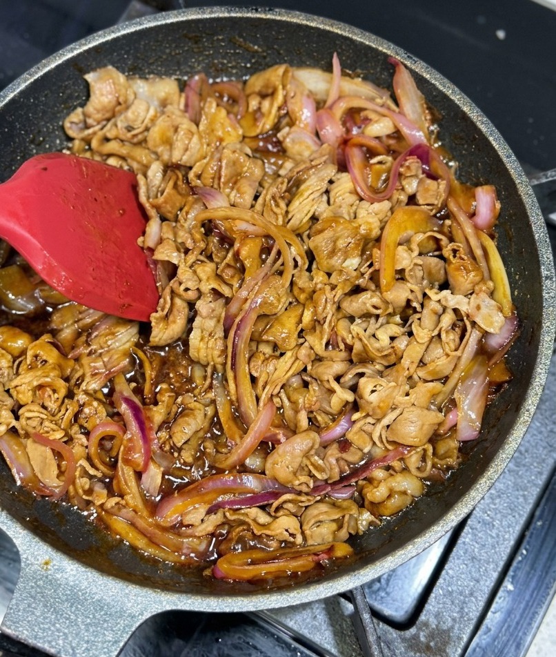 진하고 반짝이는 갈색 소스가 소고기와 양파에 골고루 코팅되며 볶아지는 모습.