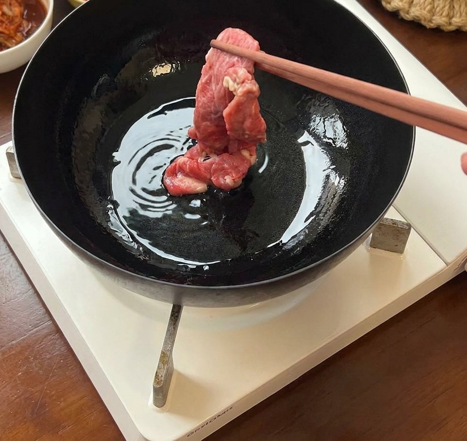 달궈진 무쇠 팬에 젓가락으로 얇은 소고기를 올려 굽는 모습.