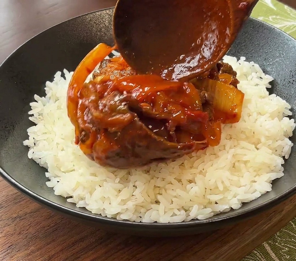 검은 세라믹 그릇에 담긴 흰 밥 위로 볶은 재료를 올리는 모습.