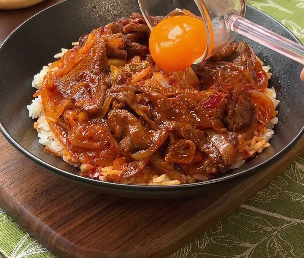 덮밥 중앙에 신선한 노란 노른자를 조심스럽게 올리는 모습.