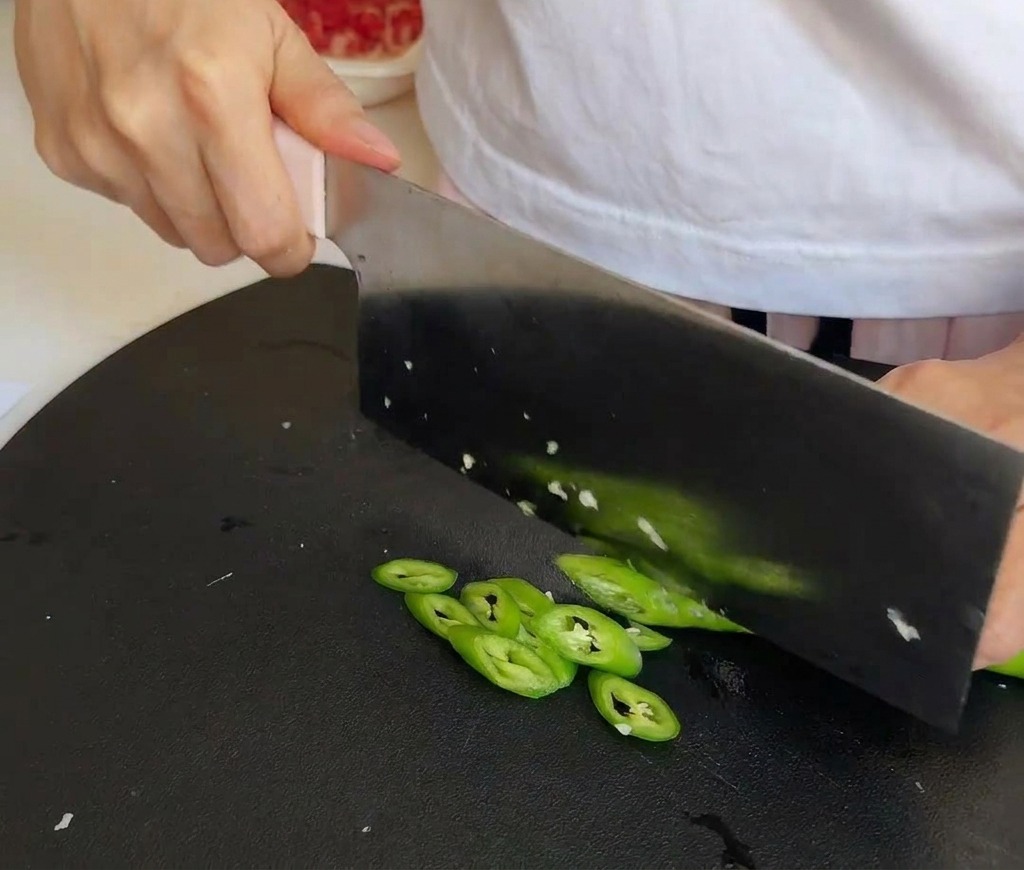 검은색 도마 위에서 중식도로 초록색 고추를 얇게 썰고 있는 모습