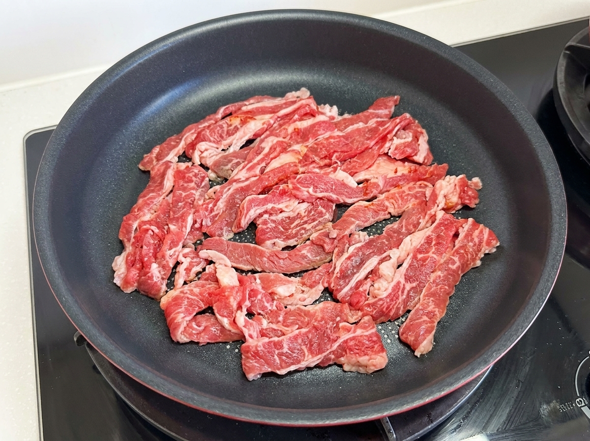 가스레인지 위 프라이팬에 펼쳐진 얇은 차돌박이 생고기