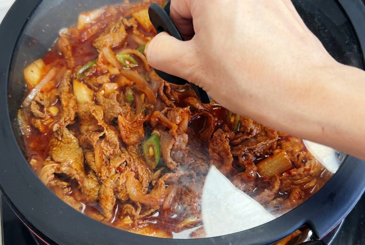 양념이 끓고 있는 팬 위로 유리 뚜껑을 덮는 모습