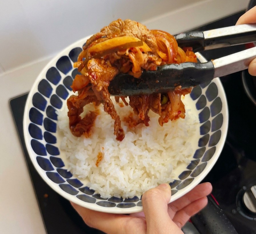 집게로 볶은 김치와 차돌박이를 흰 쌀밥 위에 얹는 모습