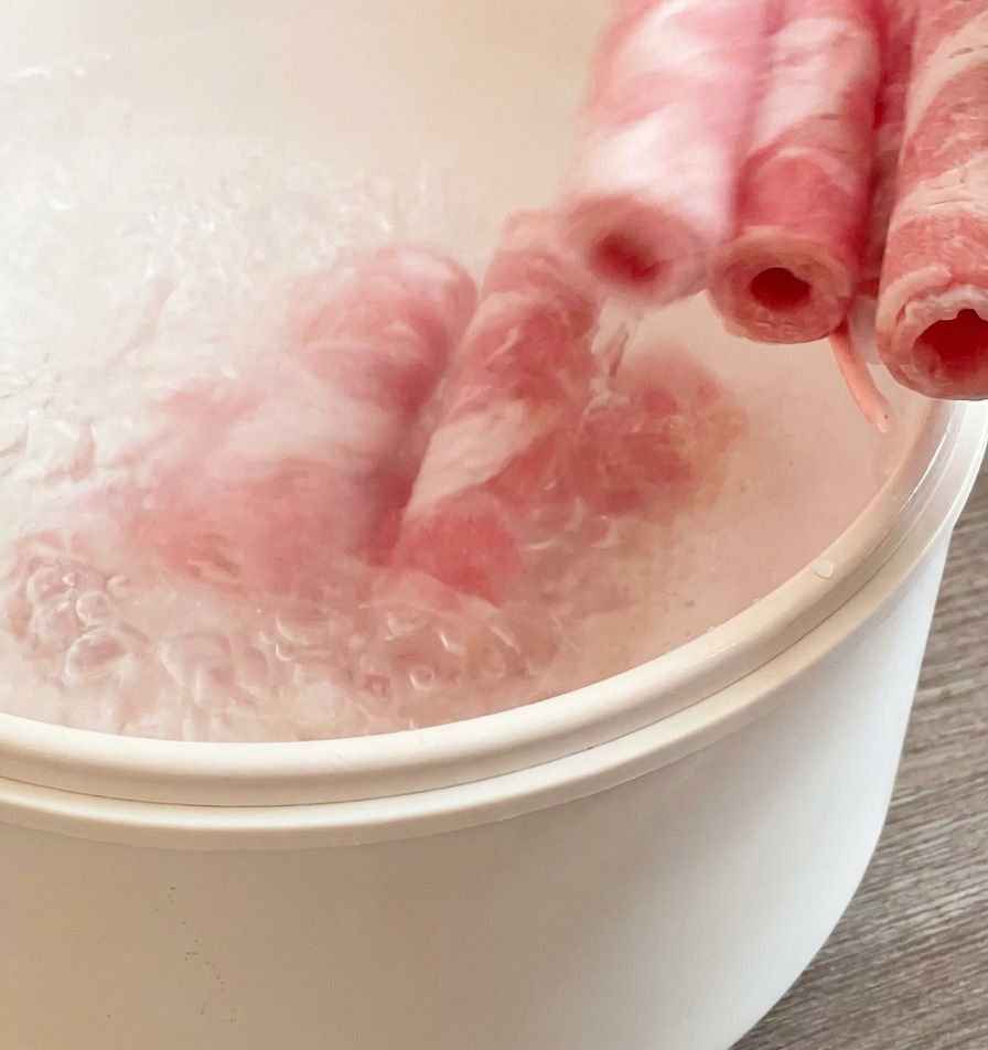 끓는 물이 담긴 흰색 냄비에 냉동 소고기를 넣어 가볍게 데치는 모습.
