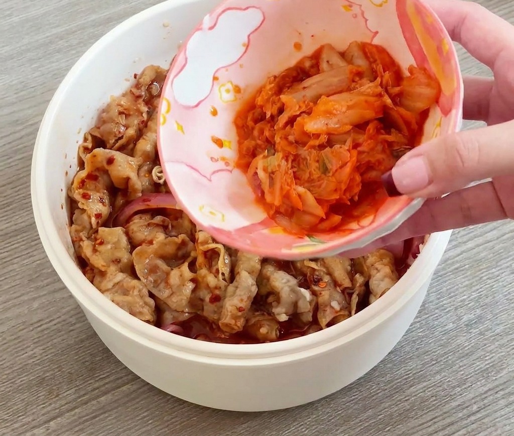 볶고 있는 소고기에 잘게 썬 김치를 한 그릇 붓는 모습.